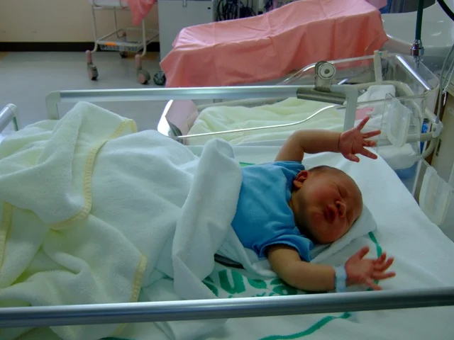 Photograph of a newborn infant with arms extended outward in a hospital bassinet, in the characteristic arm-extension phase of the Moro startle reflex