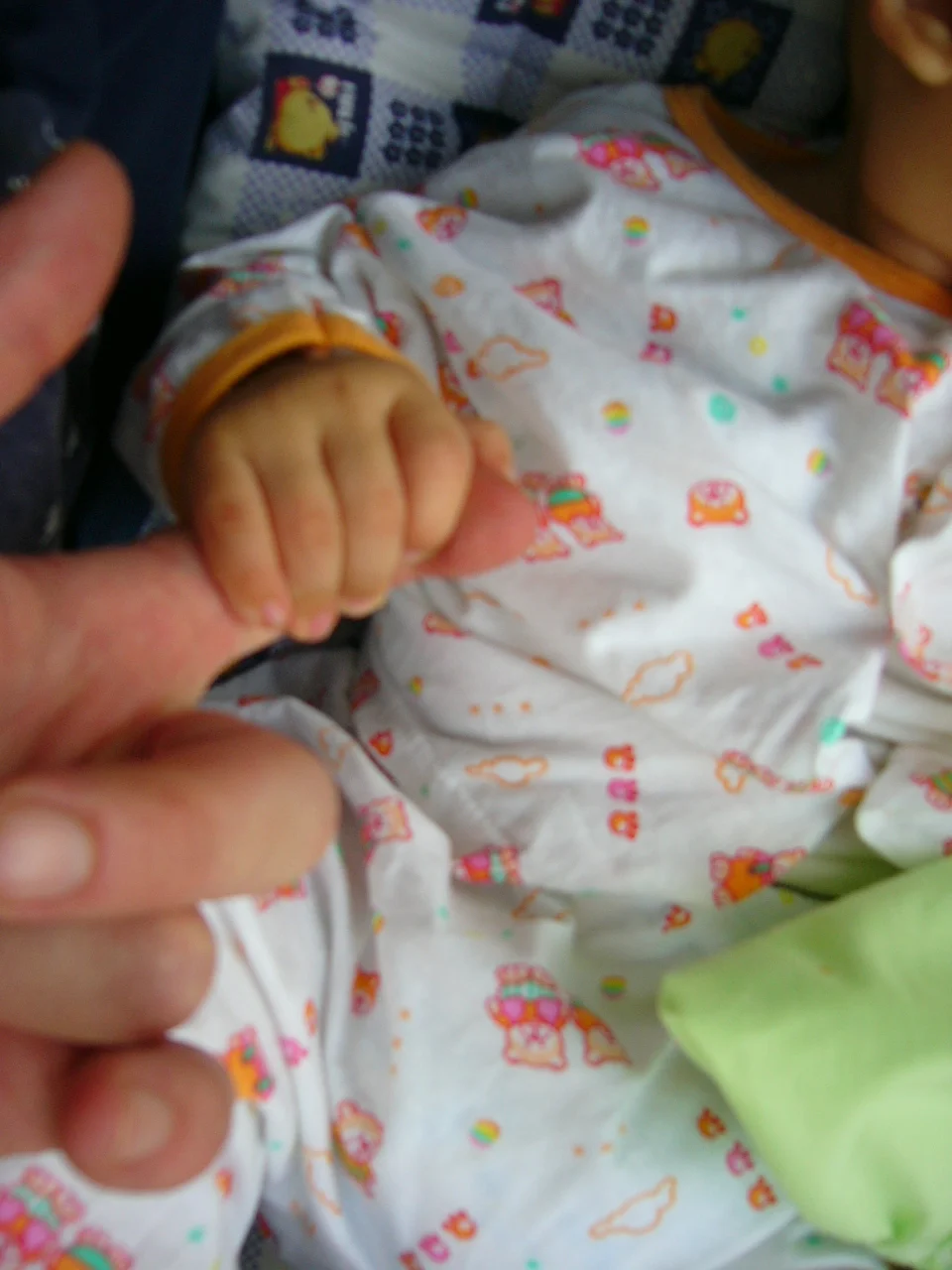 Photograph of an infant's hand tightly closed around an adult finger pressed into the baby's palm, demonstrating the palmar grasp reflex