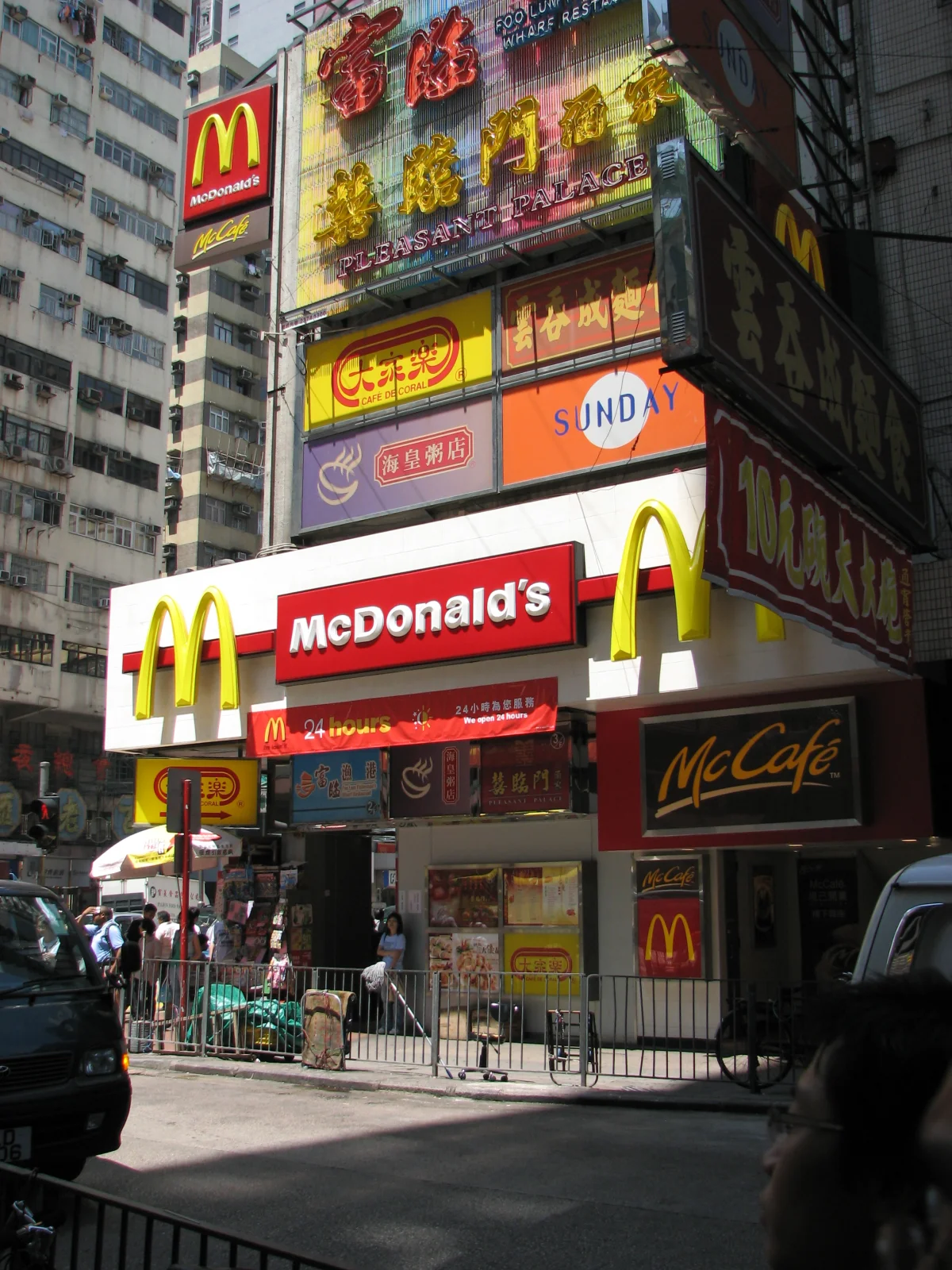 Color photograph of a multi-story McDonald's restaurant in Hong Kong with the iconic golden-arches signage in both English and Chinese characters, surrounded by other dense urban neon signage