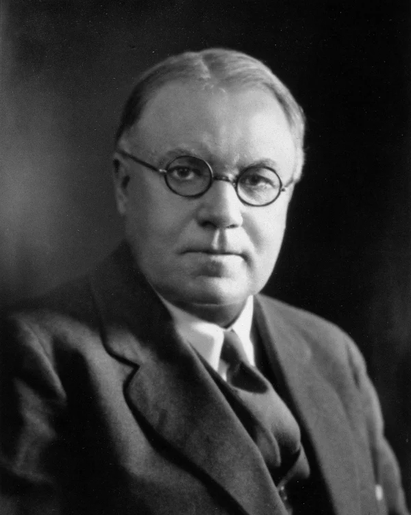 Black-and-white studio portrait of Walter Bradford Cannon in 1934, a middle-aged man with round wire-rim glasses wearing a three-piece suit