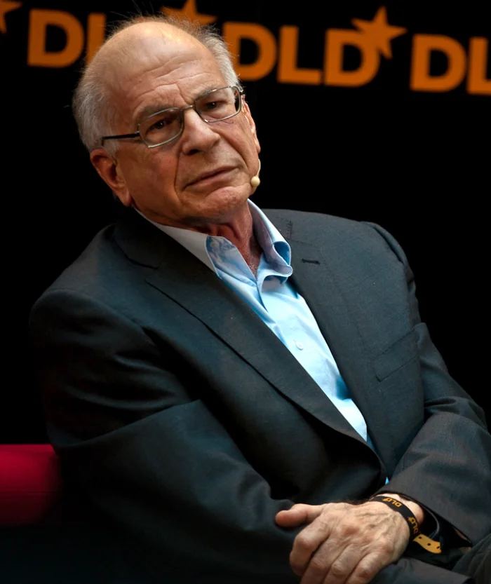Color photograph of Daniel Kahneman, an older man with gray hair and glasses, looking thoughtfully off-camera