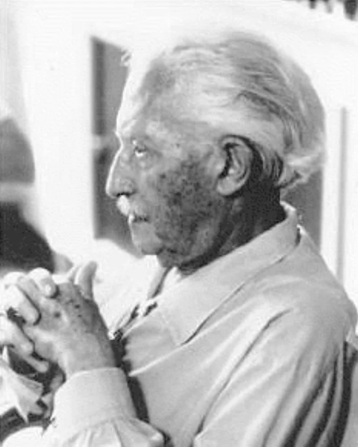 Black-and-white photograph of an elderly Erik Erikson in profile, with white hair, hands clasped in front of him, looking thoughtfully off to the left