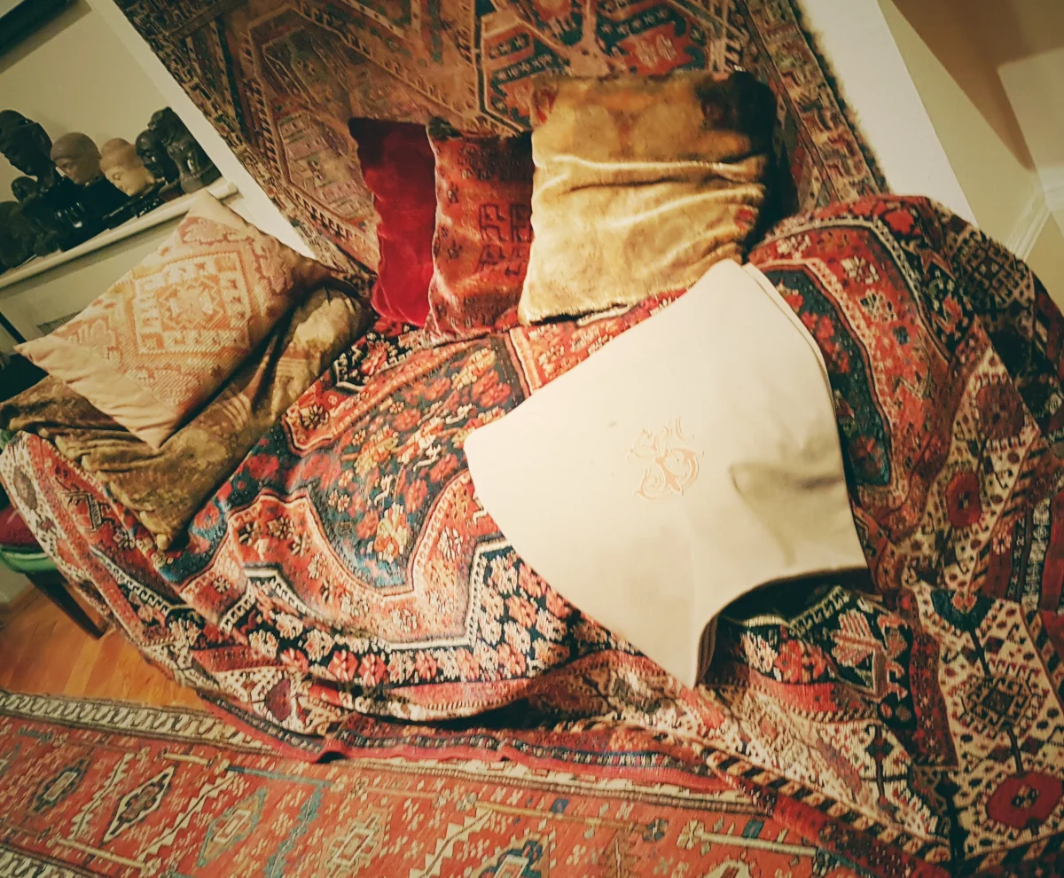 Photograph of Sigmund Freud's analytic couch, draped in an ornate Persian rug with cushions and an embroidered headrest, displayed at the Freud Museum