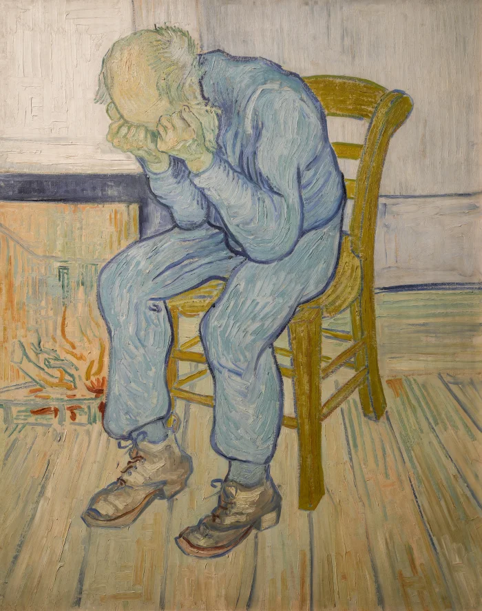 Oil painting by Vincent van Gogh titled 'At Eternity's Gate' showing an elderly bald man in a blue suit slumped in a yellow wooden chair, both hands pressed to his face in despair, in front of a small fireplace on a wooden floor. Heavy, expressive brushstrokes
