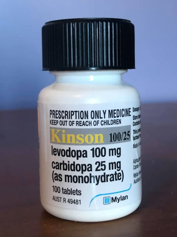 A small white prescription pill bottle with a black cap. The label reads 'PRESCRIPTION ONLY MEDICINE - KEEP OUT OF REACH OF CHILDREN' above 'Kinson 100/25, levodopa 100 mg, carbidopa 25 mg (as monohydrate), 100 tablets,' with a Mylan logo at the bottom