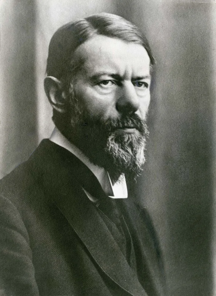 Formal black-and-white studio portrait of Max Weber from 1918, a bearded middle-aged man in a dark three-piece suit looking sternly at the camera