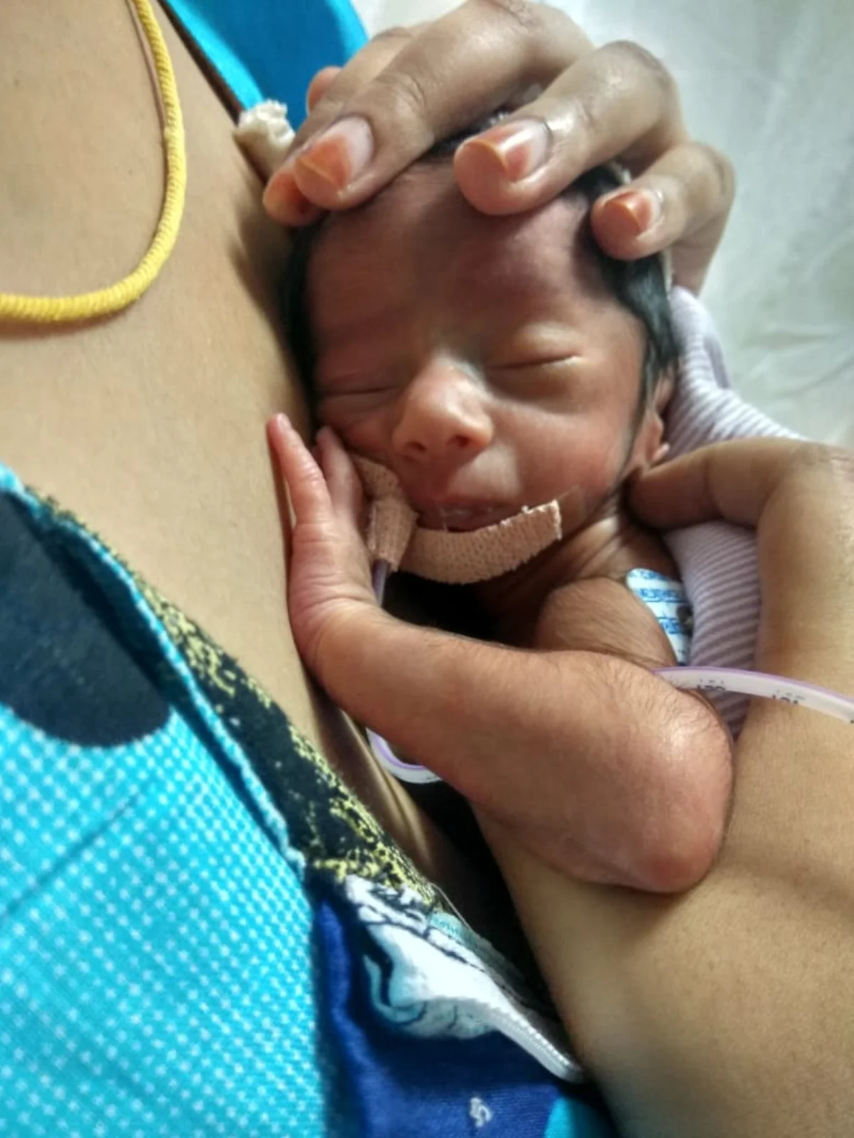 Close-up of a newborn baby resting peacefully in skin-to-skin contact on a parent's chest, the parent's hands cradling the baby's head and back