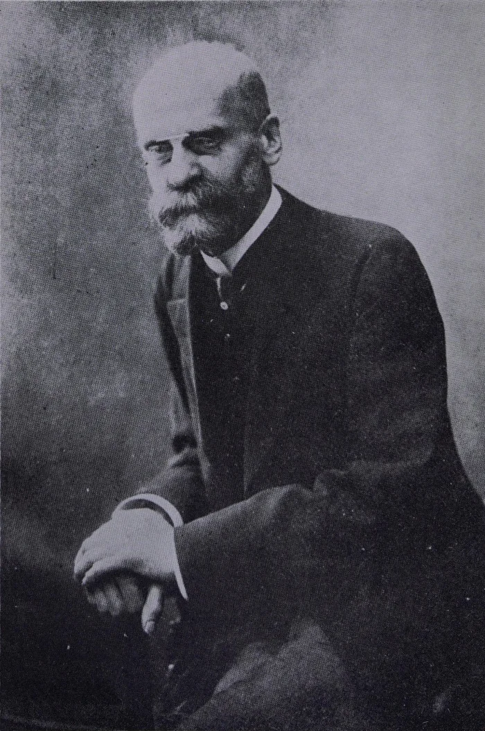 Sepia-toned formal portrait of sociologist Émile Durkheim, an older man with a receding hairline and full mustache, seated and wearing a dark suit with a crisp white shirt