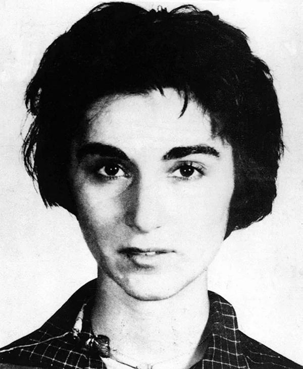 Black-and-white 1961 photograph of Kitty Genovese, a young woman with short dark hair, looking directly into the camera while wearing a checked collared shirt
