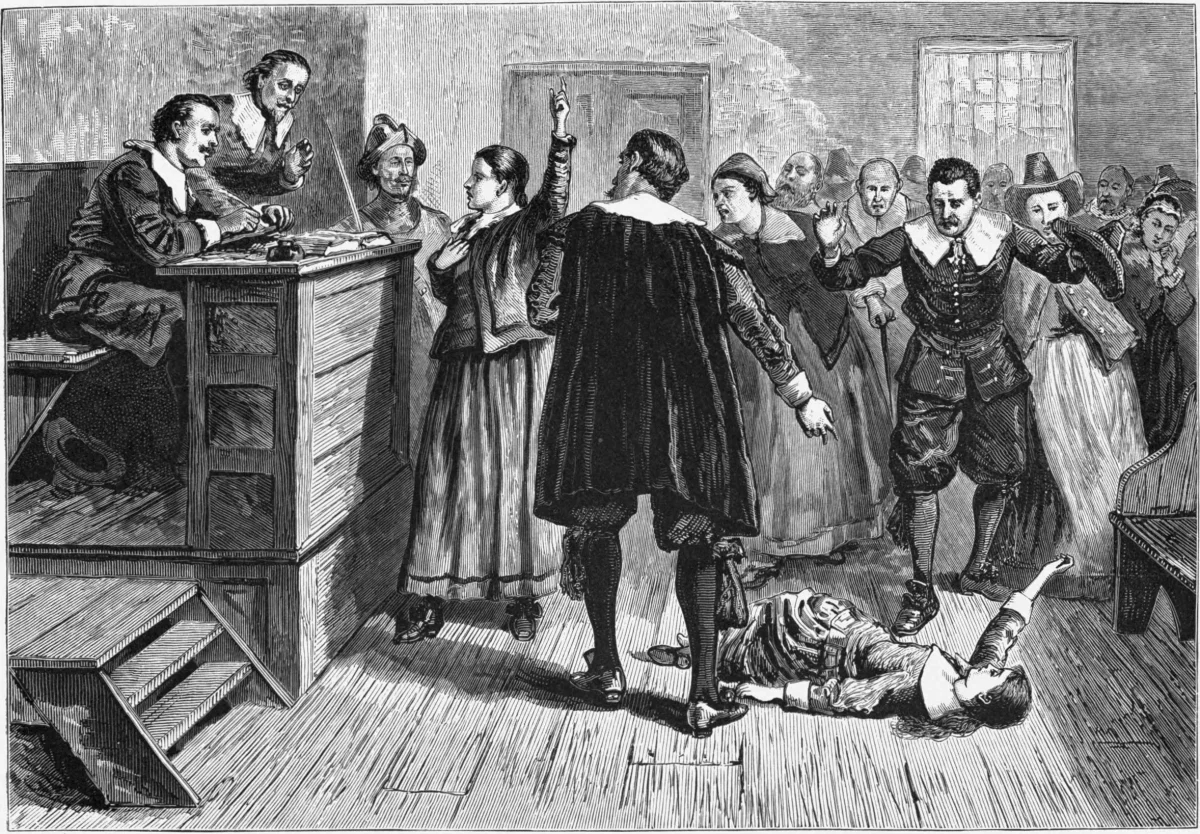 19th-century engraving of a Salem witch trial: a young woman lies sprawled on the courtroom floor as if convulsing, several women point and gesture wildly toward an accused figure, and judges in robes look on from the bench
