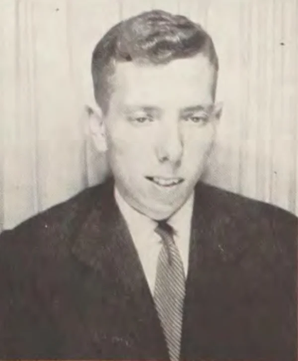 Black-and-white newspaper photograph of social psychologist Stanley Milgram in middle age, wearing a suit and patterned tie, gesturing while speaking
