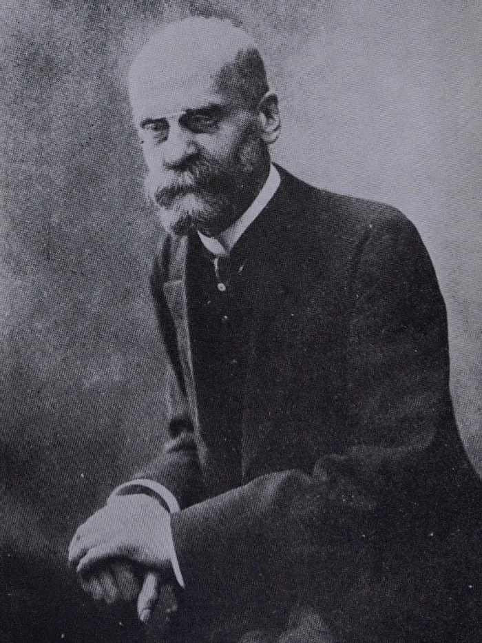 Black-and-white portrait of Emile Durkheim, a bearded man in a dark suit seated with hands folded, looking sideways with a serious expression