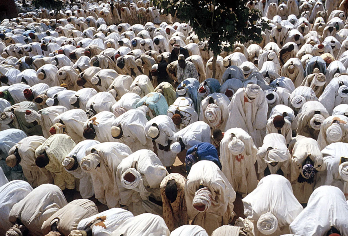 Aerial photograph of hundreds of Muslim worshippers in white robes prostrating in unison during Friday prayers at the Masallacin Bello mosque in Sokoto, Nigeria
