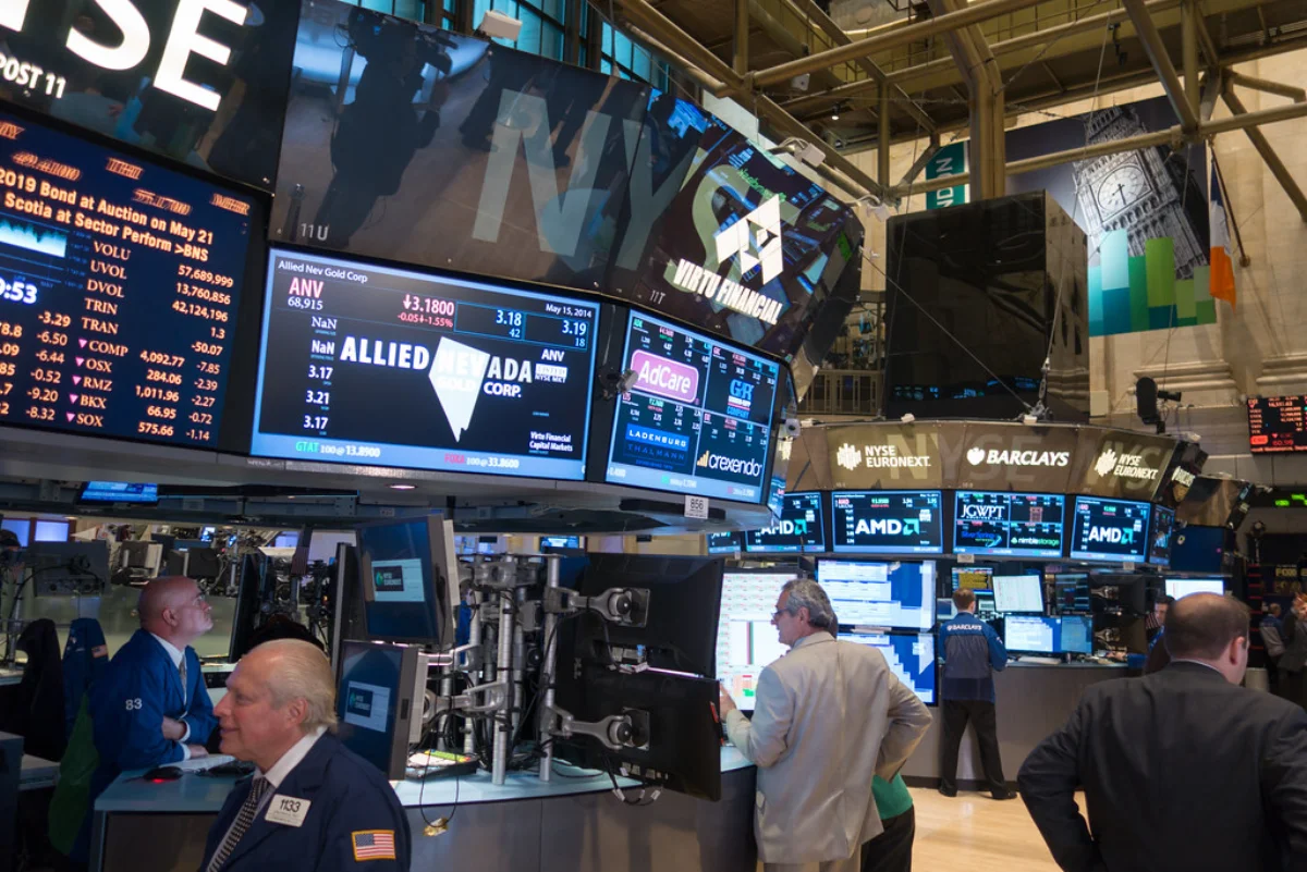 Color photograph of the trading floor of the New York Stock Exchange, with traders in jackets working amid bright LED stock-ticker displays and large screens overhead