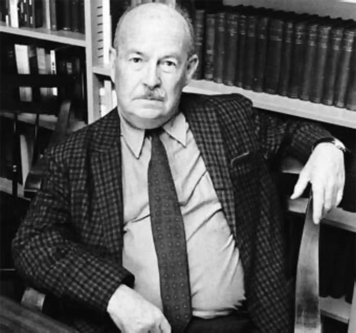 Black-and-white photograph of Talcott Parsons, an older man in academic regalia (mortarboard, gown, and university medallion), standing in front of foliage