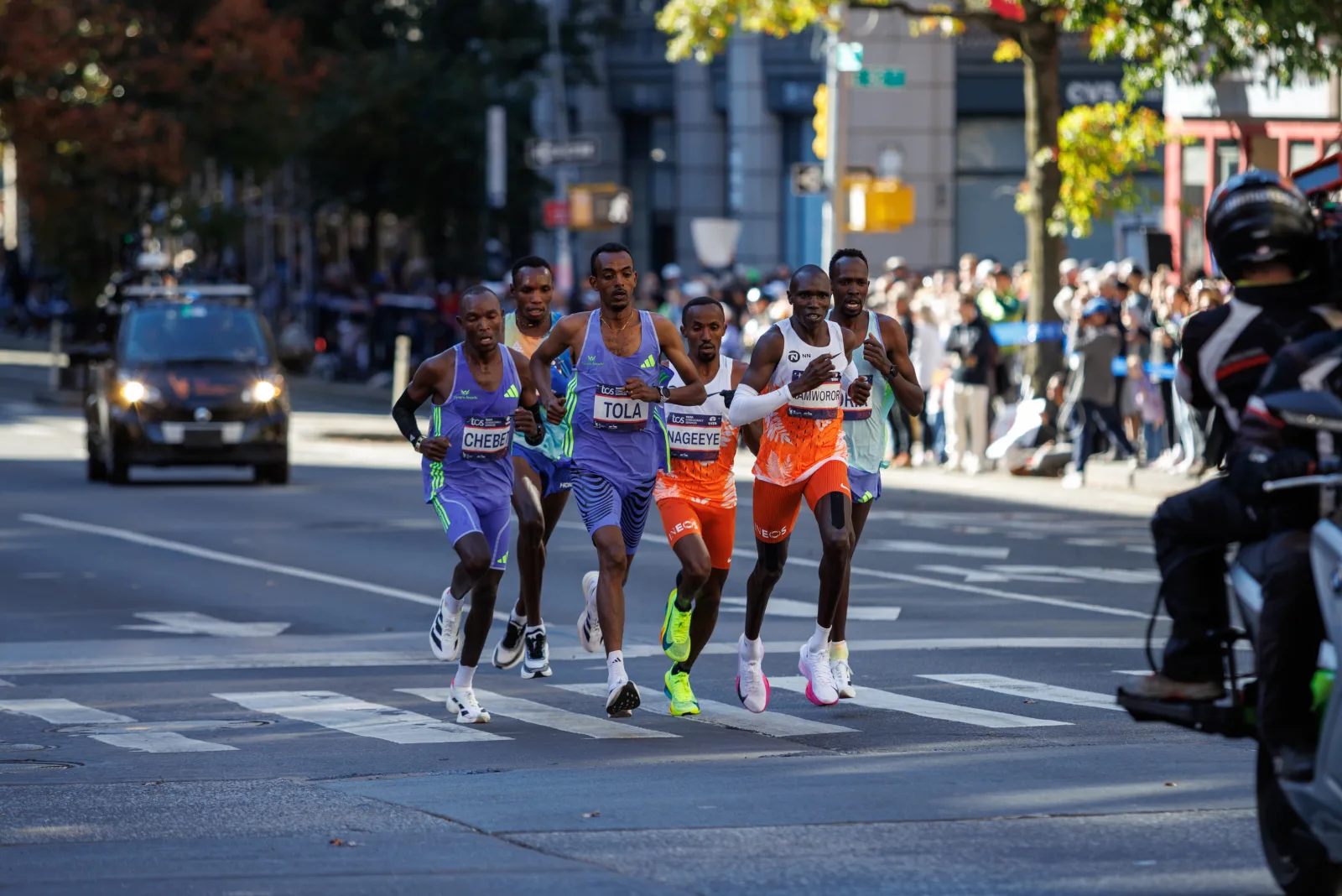 Elite marathon runners mid-race in the 2024 New York City Marathon, running in a tight lead pack down a city street
