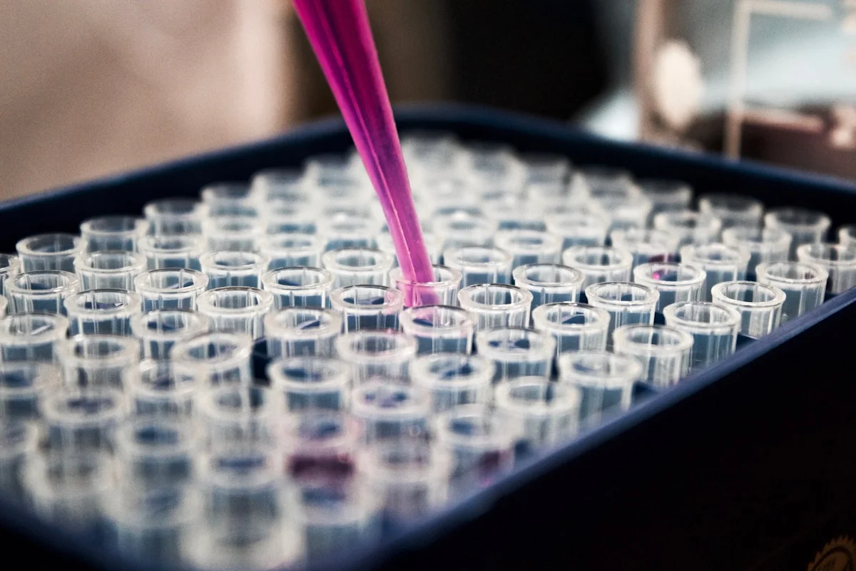 A pipette dispensing pink indicator solution into a multi-well plate in a chemistry laboratory