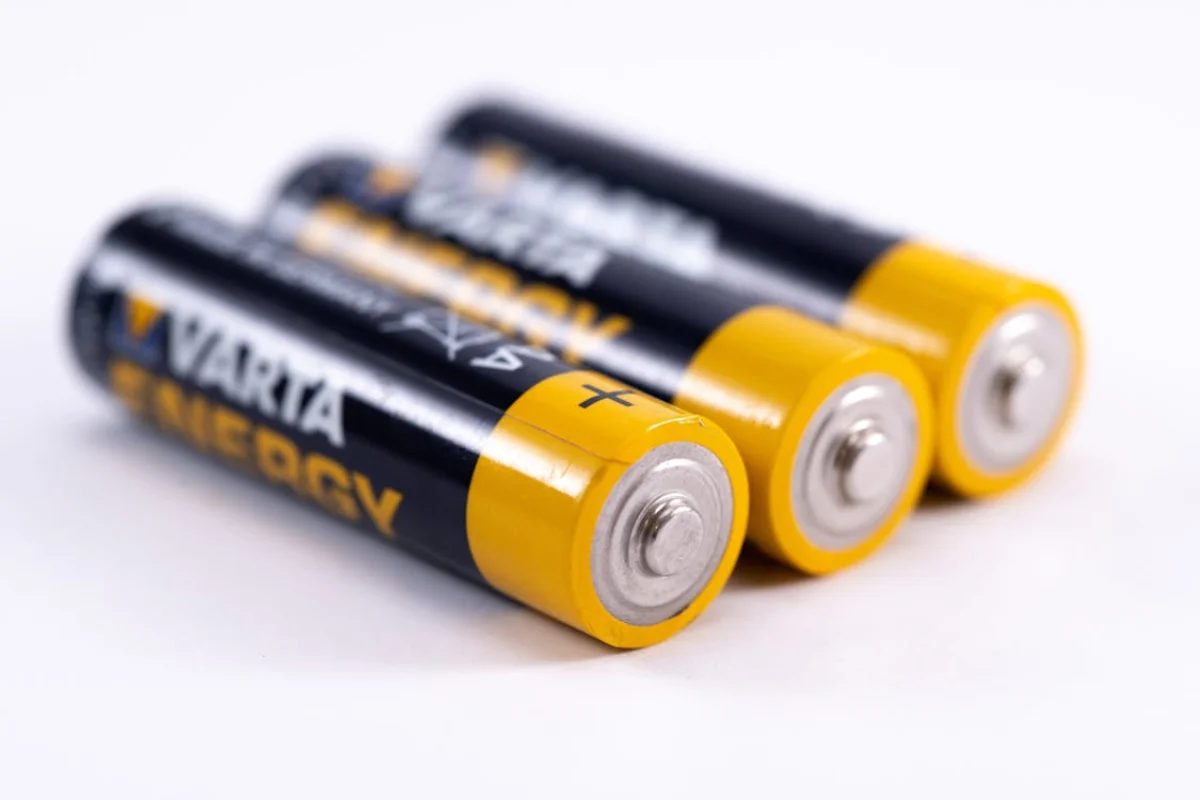 Three AA alkaline batteries lying on a white surface, showing the positive terminal ends