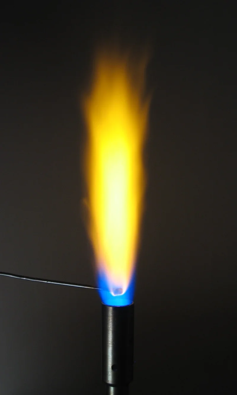 Flame test photograph showing a brilliant bright yellow-orange flame produced by sodium, with a Bunsen burner and nichrome wire loop visible