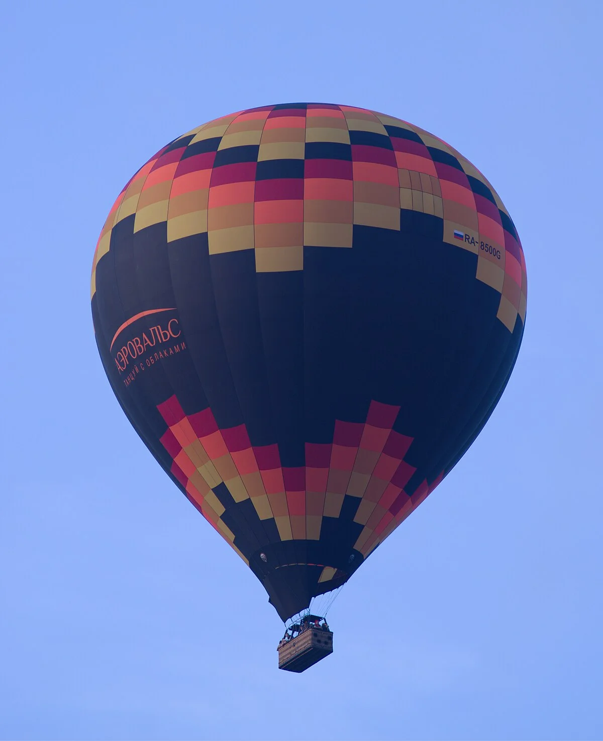 A colorful hot air balloon in flight against a clear blue sky, demonstrating Charles's law: heating the air inside the balloon causes it to expand and become less dense than the surrounding air, generating lift.